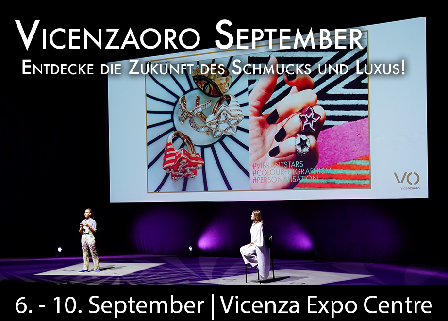 Zwei Personen auf der Bühne des Vicenza Expo Centre während der Präsentation bei Vicenzaoro September. Im Hintergrund ist eine große Leinwand zu sehen, die Schmuckstücke und eine Hand mit Ringen zeigt. Text auf dem Bild: 'Vicenzaoro September - Entdecke die Zukunft des Schmucks und Luxus! 6. - 10. September | Vicenza Expo Centre'.