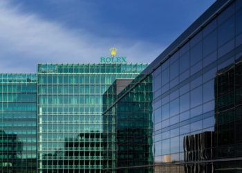 Glasfassade der Rolex-Zentrale mit Rolex-Schriftzug und Krone auf dem Dach vor blauem Himmel
