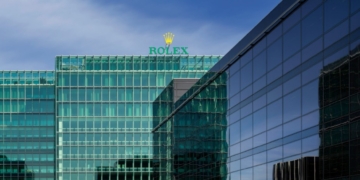 Glasfassade der Rolex-Zentrale mit Rolex-Schriftzug und Krone auf dem Dach vor blauem Himmel
